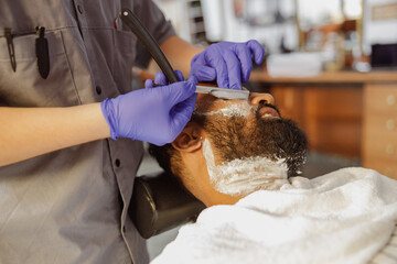 In a contemporary salon environment, a highly skilled barber meticulously shaves the beard of a...