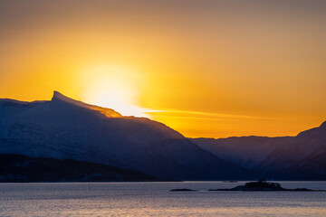 A beautiful sun shining over the snowy mountains and fjord during the first day of arctic winter. Arctic nature in Scandinavia during winter season.