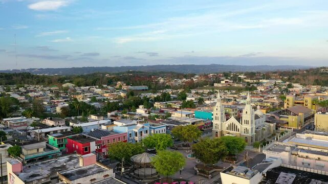 plaza and church of Aguada, Puerto Rico surrounded by the city buildings, greenery and streets