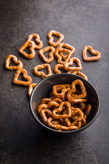 Heart shaped pretzel in bowl on black table.