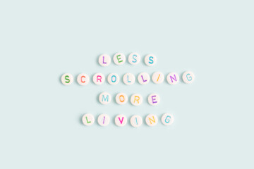 Less scrolling more living. Quote made of white round beads with multicolored letters on a blue background.