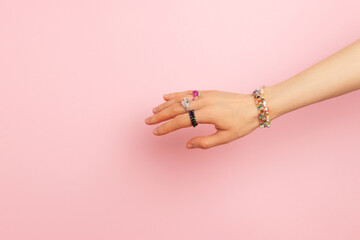 Handmade rings and bracelets on a female hand in front of pink background.