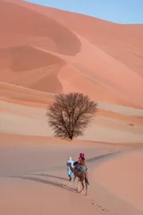Poster A woman in a red turban riding a camel across the thin sand dunes of the in Western Sahara Desert, Morocco, Africa
