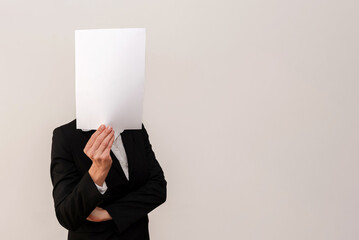 Businesswoman in suit holding blank sheet of paper in front of face on neutral background