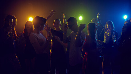 Fototapeta premium Group of energetic young people, boys and girls, enjoying lively party in a dimly-lit night club with neon lights. Spirit of youth culture and entertainment. Concept of leisure, celebration, enjoyment