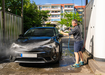 Man washes his car with water and soap at self-service car wash. Focus is on car care, keeping car clean and taking care of its appearance. Self-service concept