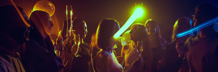 Young friends enjoying party in dimly lit room with glowing neon lights, cheerfully dancing and...