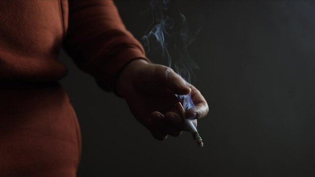 A man smokes a cigarette. Craving for smoking. A cigarette on a black background, smoke is visible. A lot of noxious smoke. Experienced smoker. This is bad for your health. Problems and depression