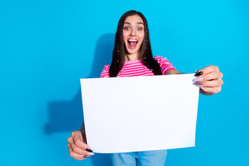 Naklejka premium Cheerful Woman Holding Blank Paper Against Vibrant Blue Backdrop, Promoting Positivity and Creativity