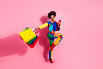 Fototapeta premium Stylish young woman in colorful outfit holding shopping bags on pink background with joyful expression