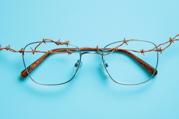 Creative photo of glasses intertwined with barbed wire on a blue background.