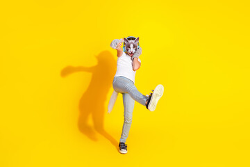 Happy young girl wearing a cat mask and stylish outfit in a playful pose on a yellow background.