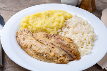Grilled tilapia or saint peter with rice and mashed potato over wooden table