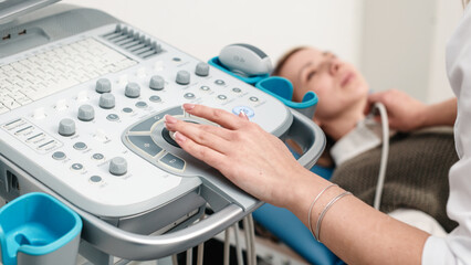 A doctor in blue gloves performs a thyroid ultrasound, moving the probe on a young patient’s...