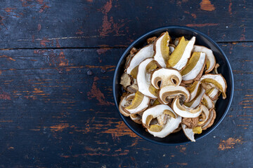dried boletus mushrooms in a cup on old black vintage background with copy space, top view