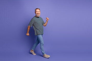 Happy mature man with a beard walking joyfully in casual attire against a vibrant purple background