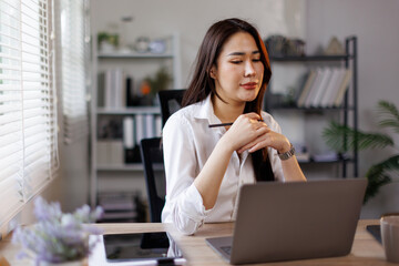 Portrait of asian woman accountant smiles while analyzing financial data on her laptop and using a calculator in a bright office setting
