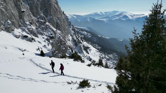Couple hiking in the snow-covered Bucegi Mountains of Romania during winter on a sunny day