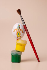 egg with a rabbit pattern, jars of paint and brushes on a beige background
