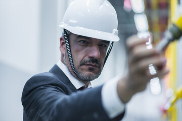 Business professional in safety gear inspects industrial equipment during operational assessment at...