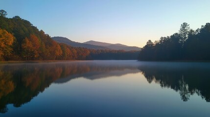 Obraz premium Serene Mountain Lake at Dawn: A tranquil scene of a misty mountain lake reflecting the vibrant hues of autumn foliage against a serene sunrise sky. The air hangs heavy with the promise of a new day.