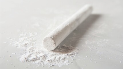 A single white chalk stick with subtle dust particles around it, lying on a smooth white surface.