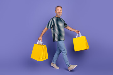 Happy senior man enjoying shopping with colorful yellow bags against a vibrant purple background