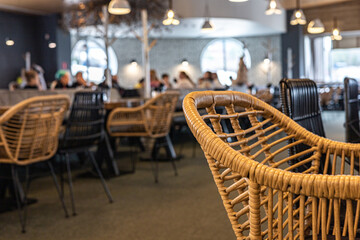 Wicker chair in a modern cafe with a bustling and lively environment, blurred view of chairs, tables, and people. Contemporary cafe design, highlighting the use of natural materials 