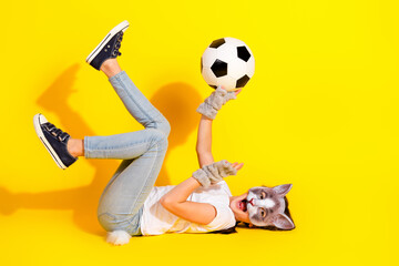 Young girl wearing a cat mask plays with a soccer ball on a vibrant yellow background, showcasing creativity and fun.