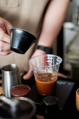 barista is preparing coffee drink by pouring espresso into clear plastic cup, showcasing close up of process with focus on rich color of coffee