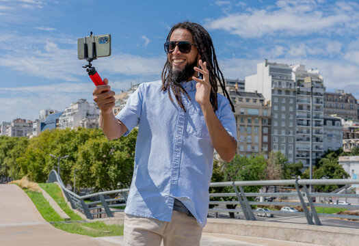 Young Latino man waves while vlogging with a smartphone 
