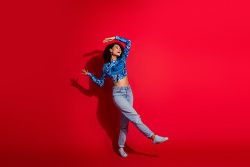 Stylish young woman posing in colorful modern attire on a vibrant red backdrop expressing energy and joy.