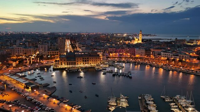 Aerial sunset view of Bari city lights and marina with yachts. Flight over the old town and the embankment of Bari, Puglia, Italy