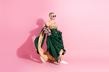 Fototapeta premium Elegant woman in medieval dress with modern sneakers on pastel pink background, blending historical and contemporary fashion