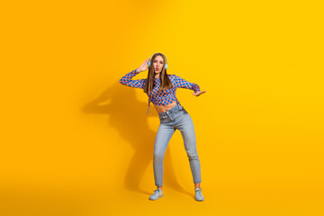 Trendy young woman with headphones dancing in casual jeans and printed top on vibrant yellow background
