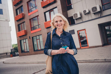 Smiling elderly woman in denim dress enjoying a casual walk through the urban city streets