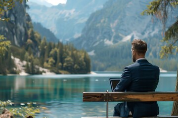 Fototapeta premium Businessman working remotely by the serene lakeside with stunning mountain views.