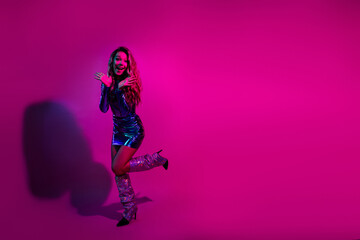 Joyful woman in a shiny blue dress celebrating against a vibrant pink background, expressing happiness and charm.
