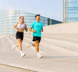 Couple jogging together on urban steps during a sunny day in a modern architectural setting