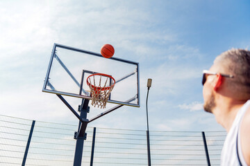 Basketball player shooting a ball towards the hoop on a sunny day at an outdoor court