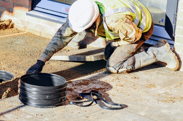 Worker laying paving slab near building entrance during daytime in a construction site with safety gear