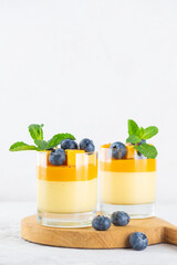 Mango panna cotta mousse pudding with blueberries and mint on a wooden board. Vegan food, sugar,...
