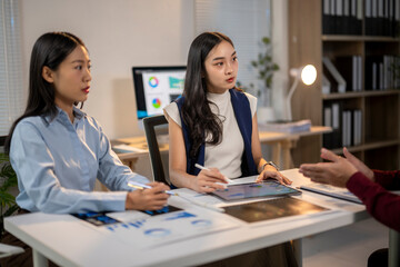 Two women are sitting at a desk with a white board and a tablet