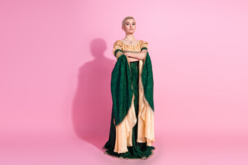 Fototapeta premium Elegant young woman in historical costume standing confidently against a pink background