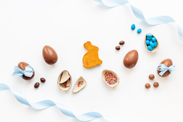 Various chocolate Easter eggs, cracked chocolates and a wrapped easter egg with blue ribbon