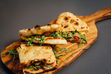 Close up of Pizza-Sandwich with Veal and Roasted Pepper – A delicious fusion of seared veal slices, roasted pepper, sun-dried tomatoes, arugula, parmesan cheese, cheddar, capers, and pesto sauce 