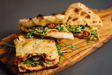 Veal and Roasted Pepper Pizza-Sandwich with sun-dried tomatoes, arugula, Parmesan, Cheddar, capers, and pesto sauce on a crispy flatbread. A gourmet Italian-inspired dish with a rustic presentation.
