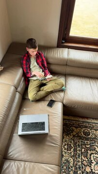 Boy using laptop and phone on a couch in a cozy room