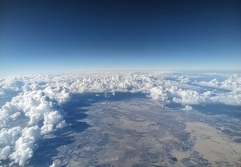 Above the Clouds: Aerial View of Soft White Clouds Over Expansive Landscape with Blue Sky as a Backdrop and Earthly Features Below