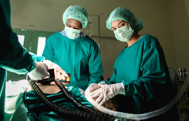 Professional males and female medical team using defibrillator perform during critical surgical...